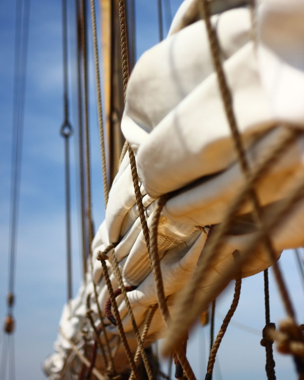 Traditional sail flaked and laced to its boom, natural-fibre rope in the foreground